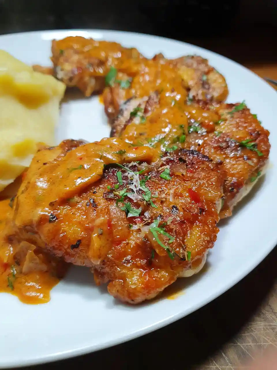 A close-up photo of a plate of chicken thighs covered in a glossy orange sauce and garnished with chopped green herbs…