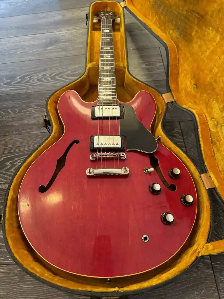 A red semi-hollow body electric guitar with a black pickguard and two humbucker pickups sits inside an open, yellow…