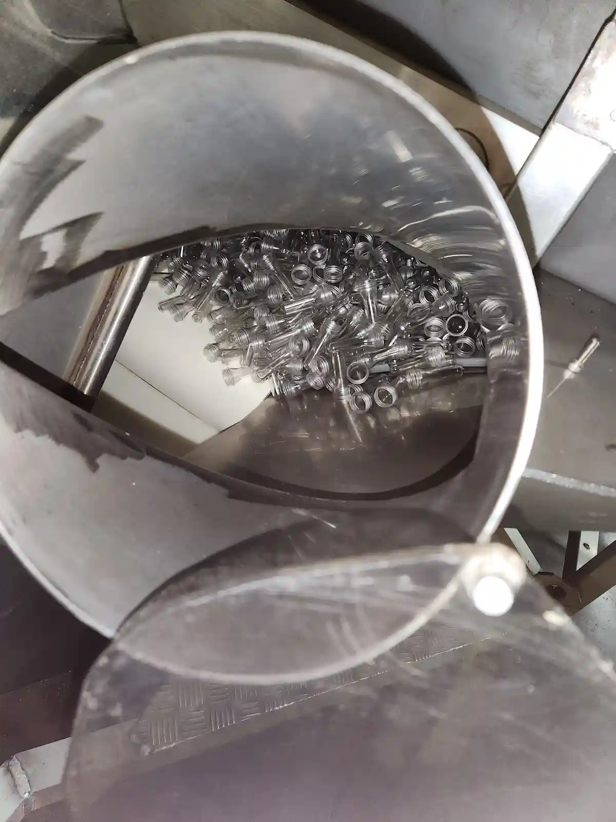 A top-down view of a large metal bucket filled with numerous clear plastic vape cartridges, with a clear plastic lid…