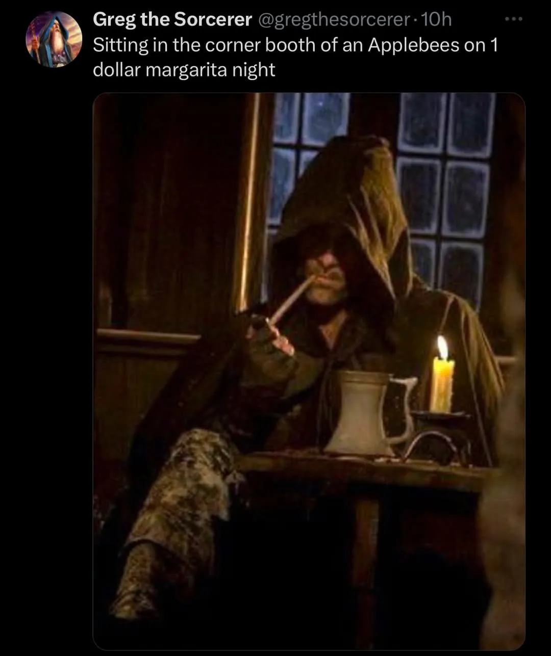 A person in a dark hooded robe sits at a wooden table in a dimly lit room, smoking a pipe. A lit candle and a white ceramic…