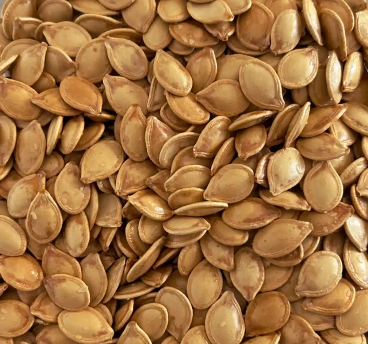 A close-up image shows a large pile of roasted, golden-brown pumpkin seeds with visible salt crystals. Overlaid text in a…