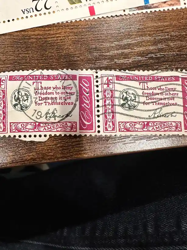 A close-up photo shows two vintage 4-cent U.S. postage stamps from 1961, each printed with the phrase 'Those who Deny…