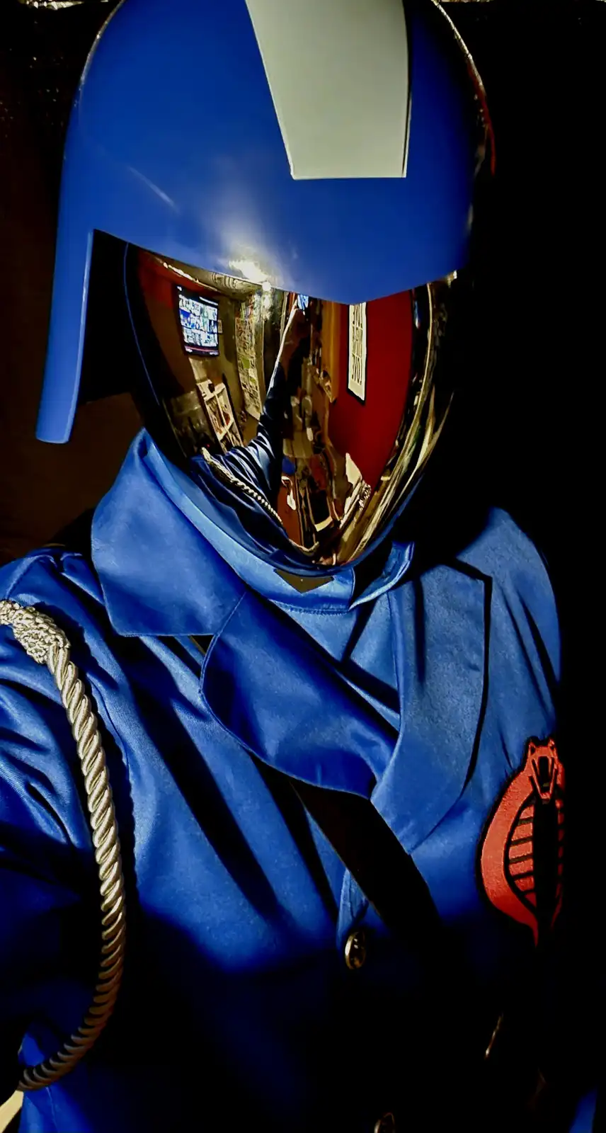 A person in a blue Cobra Commander costume from G.I. Joe, wearing a shiny gold visor helmet with a white stripe, a blue…