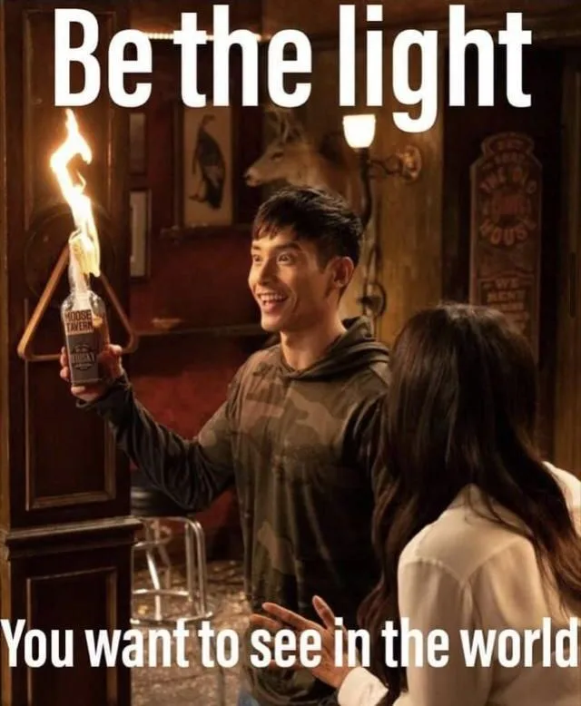 A man in a camouflage hoodie holds a bottle of liquor on fire, smiling at a woman in a white shirt. The text reads 'Be the…