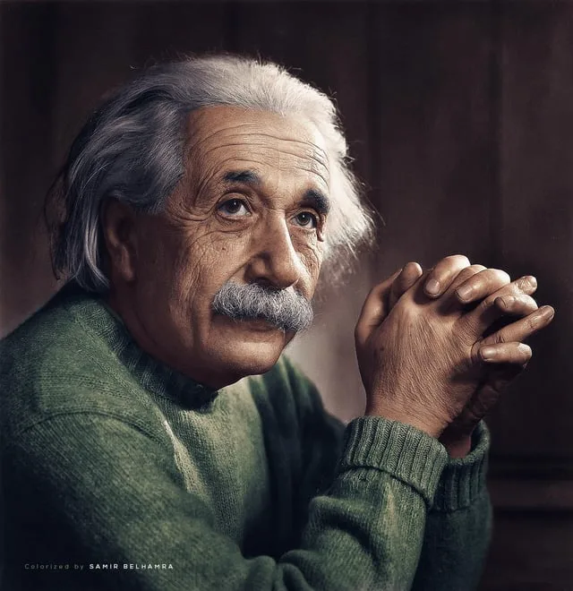 A colorized portrait of Albert Einstein, with his characteristic wild white hair and mustache, wearing a green sweater and…
