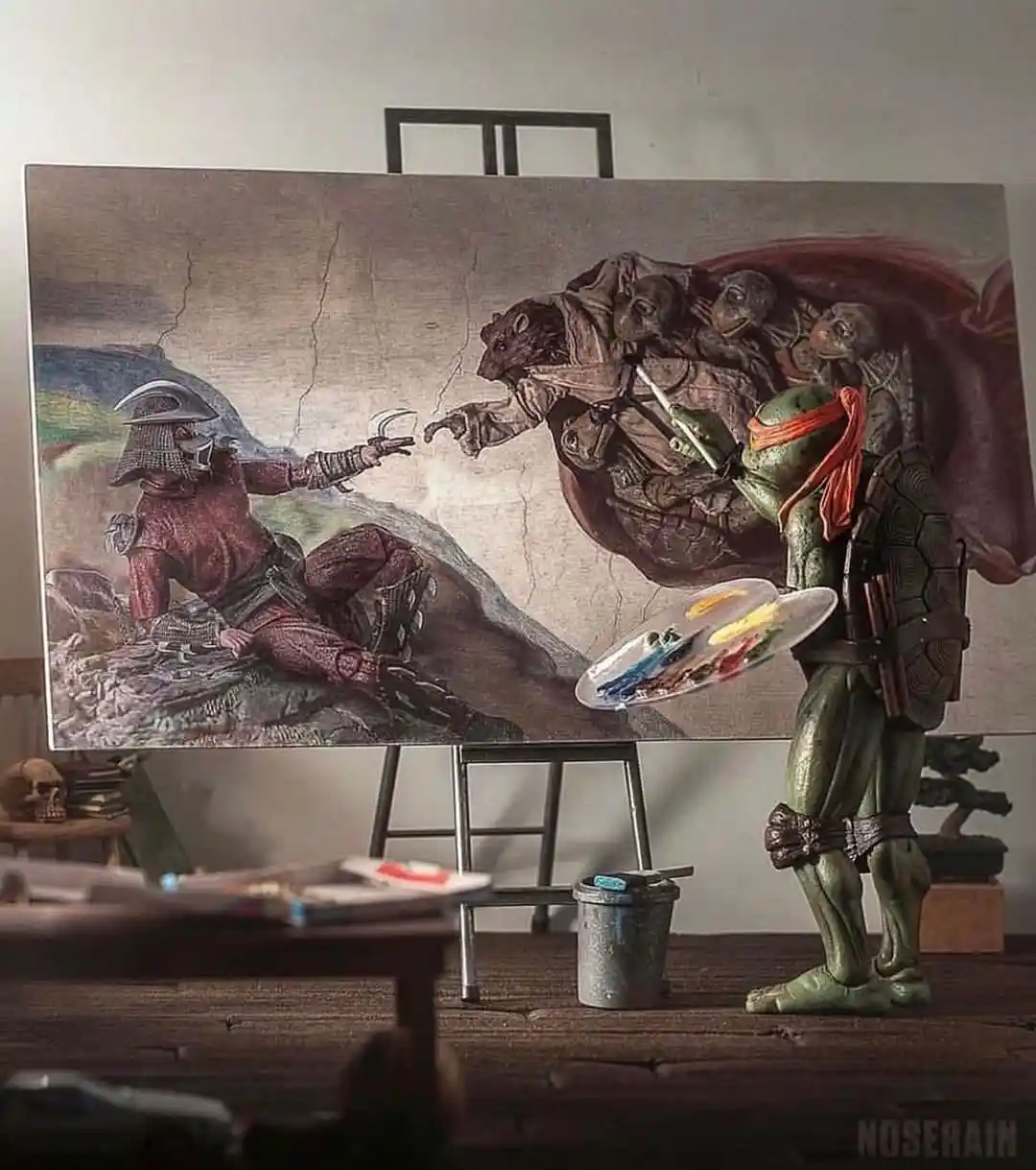 A green ninja turtle figurine, holding a paintbrush and palette, stands before an easel painting a scene resembling…