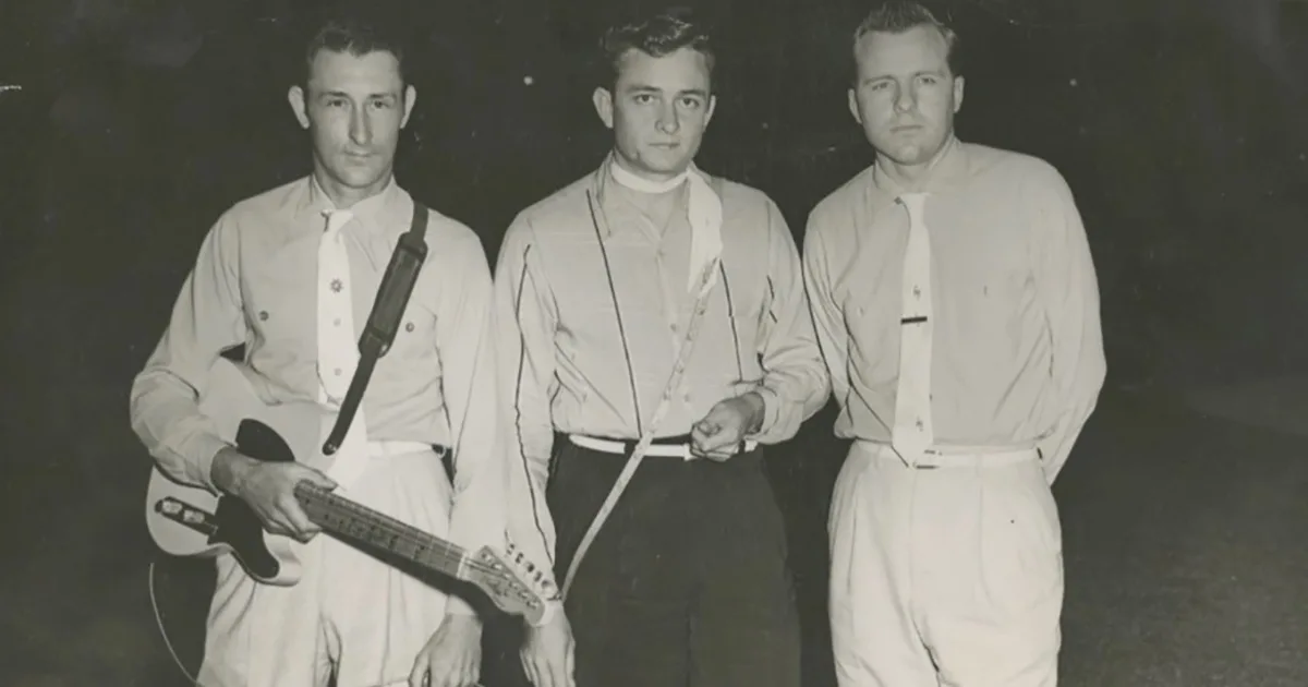 A vintage black-and-white photo shows three men in mid-20th century attire standing side-by-side. The man on the left holds…