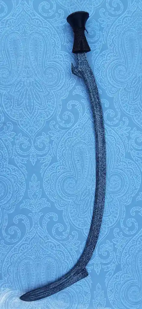 A curved, dark-colored sword with a black, textured grip lies diagonally on a light blue wallpaper featuring intricate…