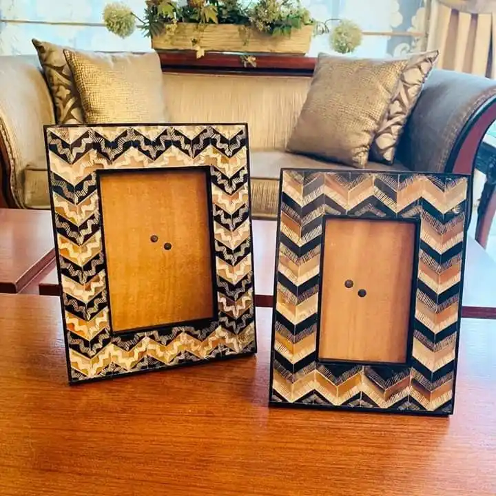 Two identical empty picture frames with a zigzag pattern sit side by side on a wooden table. The frames have a brown and…