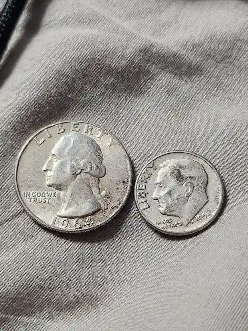 Two U.S. coins, a 1964 quarter with George Washington's profile and a 1963 half dollar with John F. Kennedy's profile, are…