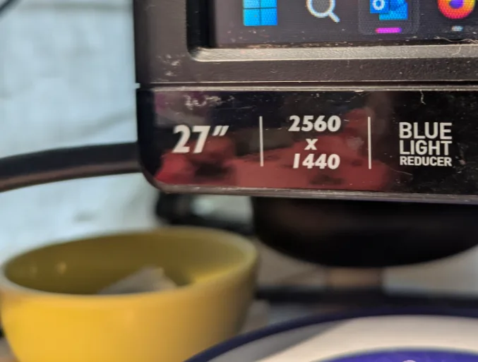 A close-up photo of the bottom bezel of a 27-inch computer monitor displaying its specs: 2560 x 1440 resolution and 'BLUE…