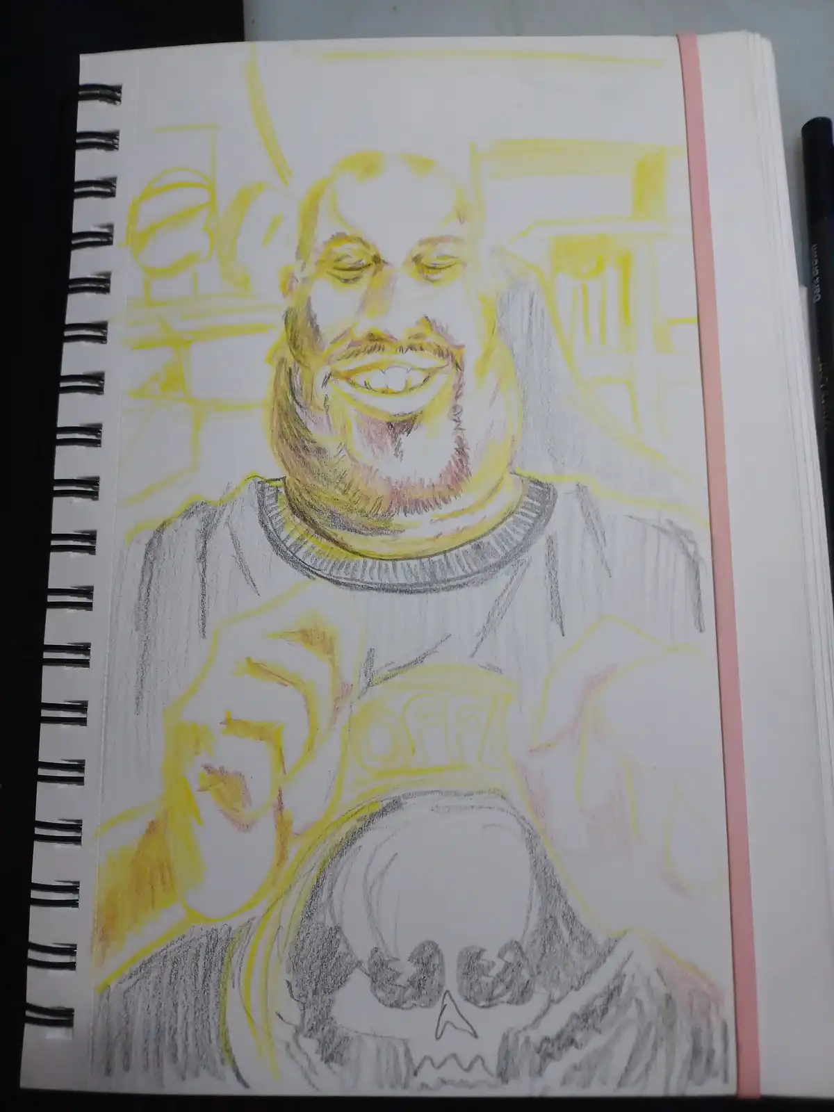 A hand-drawn sketch in a spiral-bound notebook shows a man with a wide, toothy grin and a beard, wearing a shirt with the…