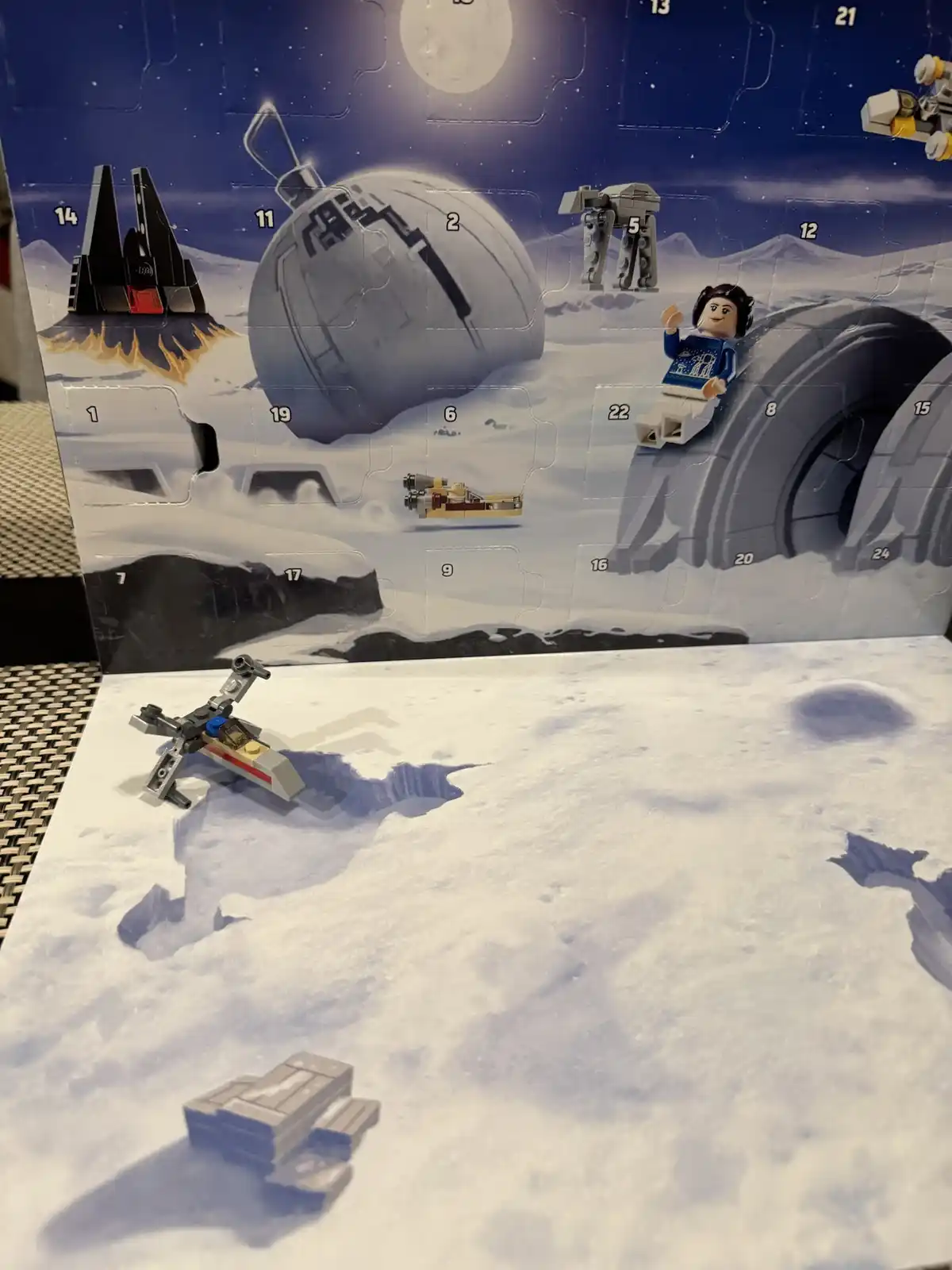 A Lego Star Wars Advent Calendar backdrop featuring snow-covered Hoth with numbered flaps and characters like Princess Leia…