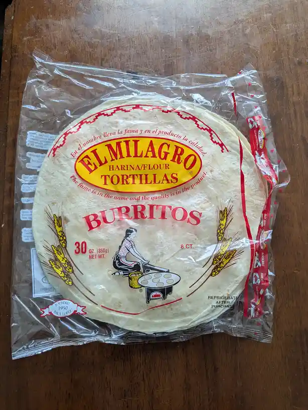 A package of El Milagro flour tortillas, labeled for burritos, sits on a wooden table. The packaging features a vintage…