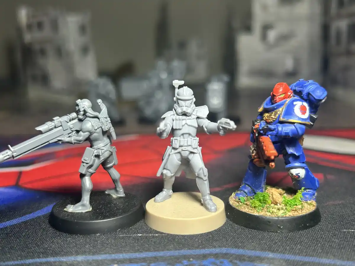 Three unpainted and painted miniature figurines stand side by side on a gaming mat; the left and center figures are grey…