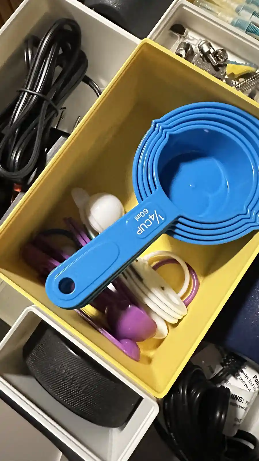 A blue 1/4 cup measuring cup is prominently displayed in a yellow storage bin, surrounded by various other kitchen utensils…