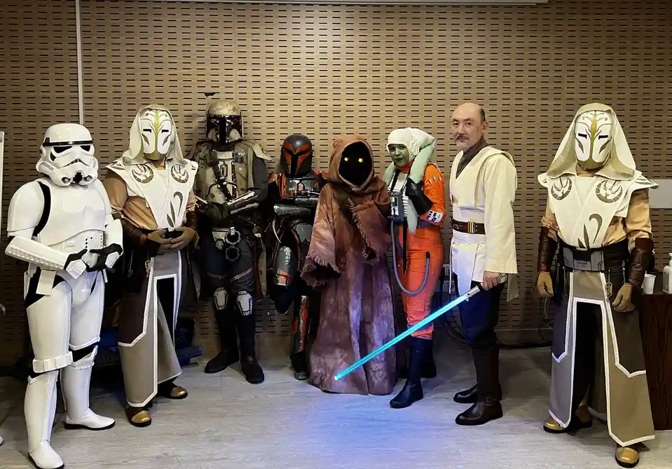 A group of people in Star Wars cosplay pose together, including a Stormtrooper, two Mandalorians, a mysterious hooded figure…
