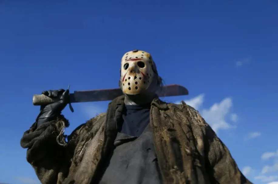 A low-angle shot shows the horror movie character Jason Voorhees wearing his iconic hockey mask and holding a large machete…