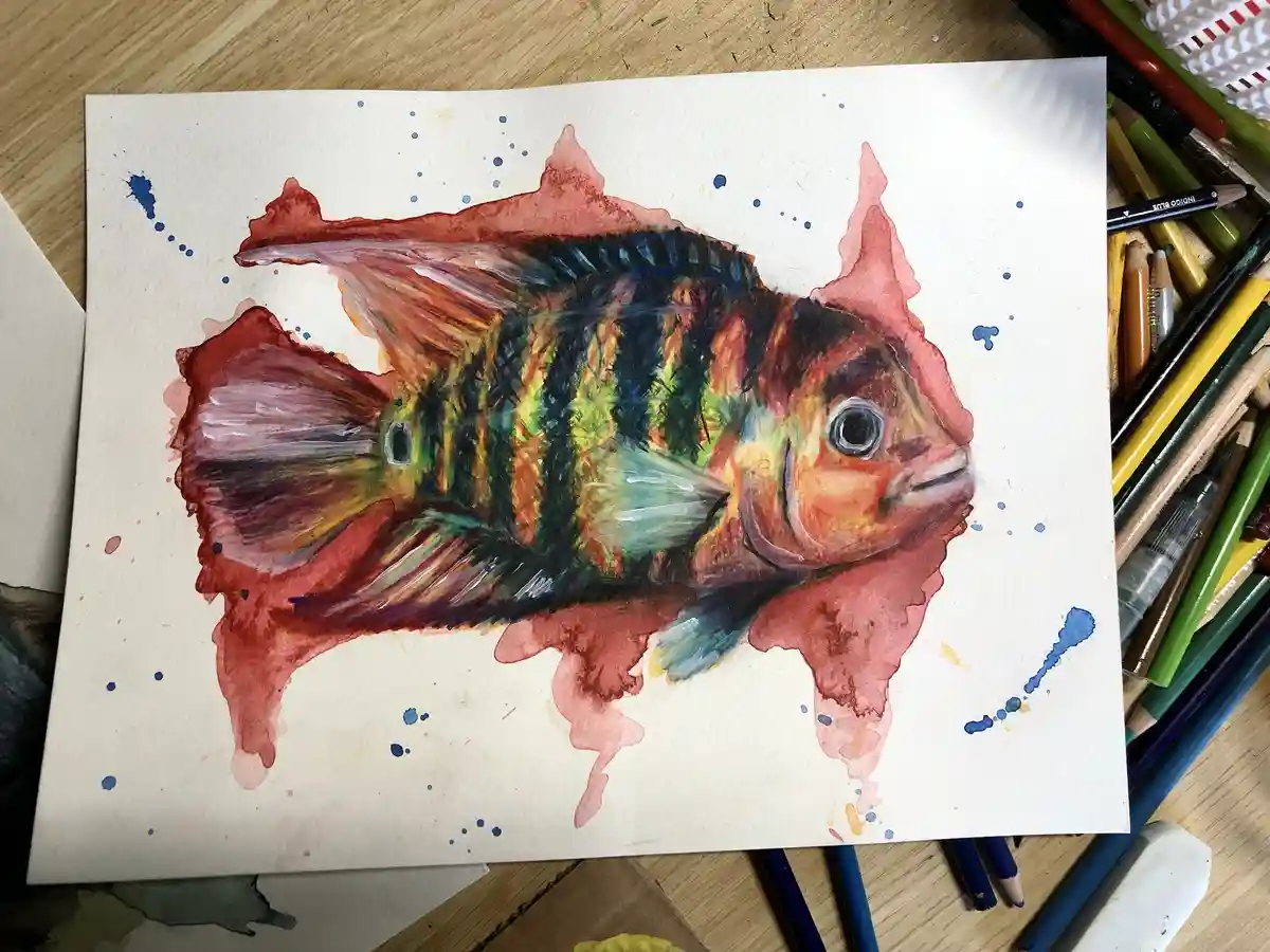 A watercolor painting of a colorful fish with red, green, and black stripes, surrounded by red and blue paint splatters on…