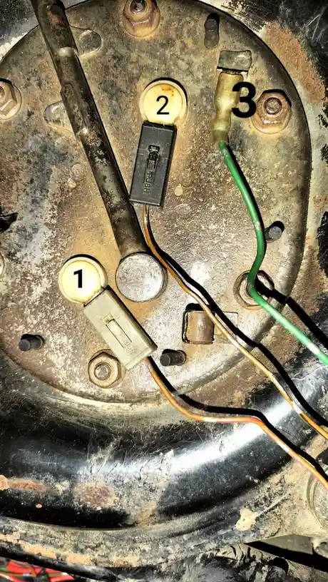 A close-up of a rusty, worn mechanical panel with three numbered components: a beige toggle switch labeled '1', a black…