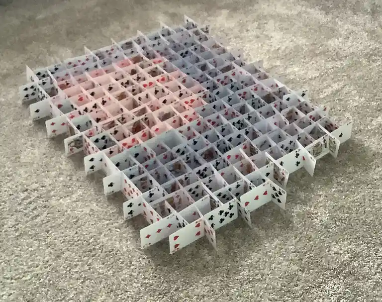A large, intricate, and remarkably stable house made entirely of playing cards, arranged in a grid pattern on a carpeted…