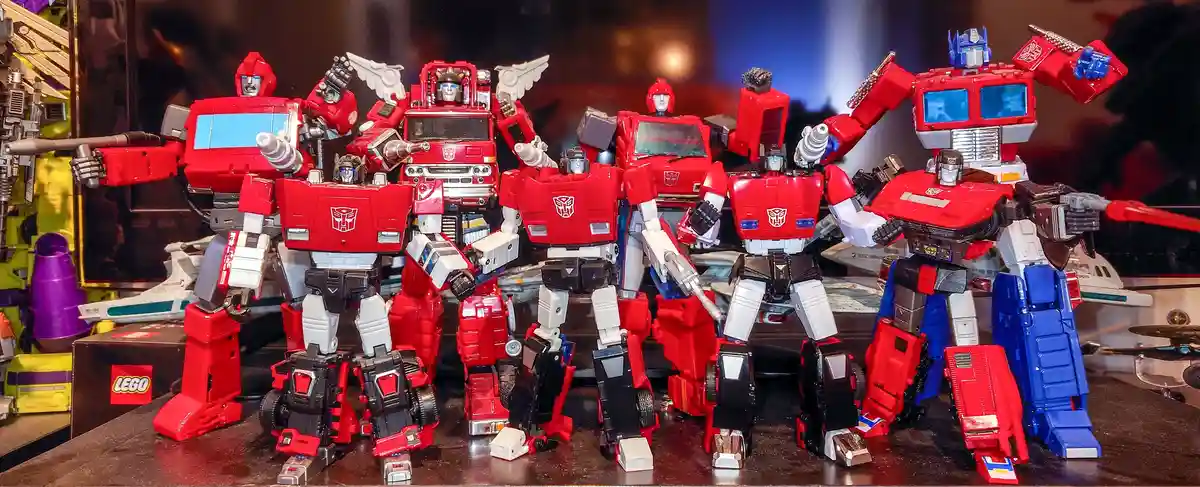 A collection of multiple red and blue Optimus Prime action figures from the Transformers franchise are displayed together on…