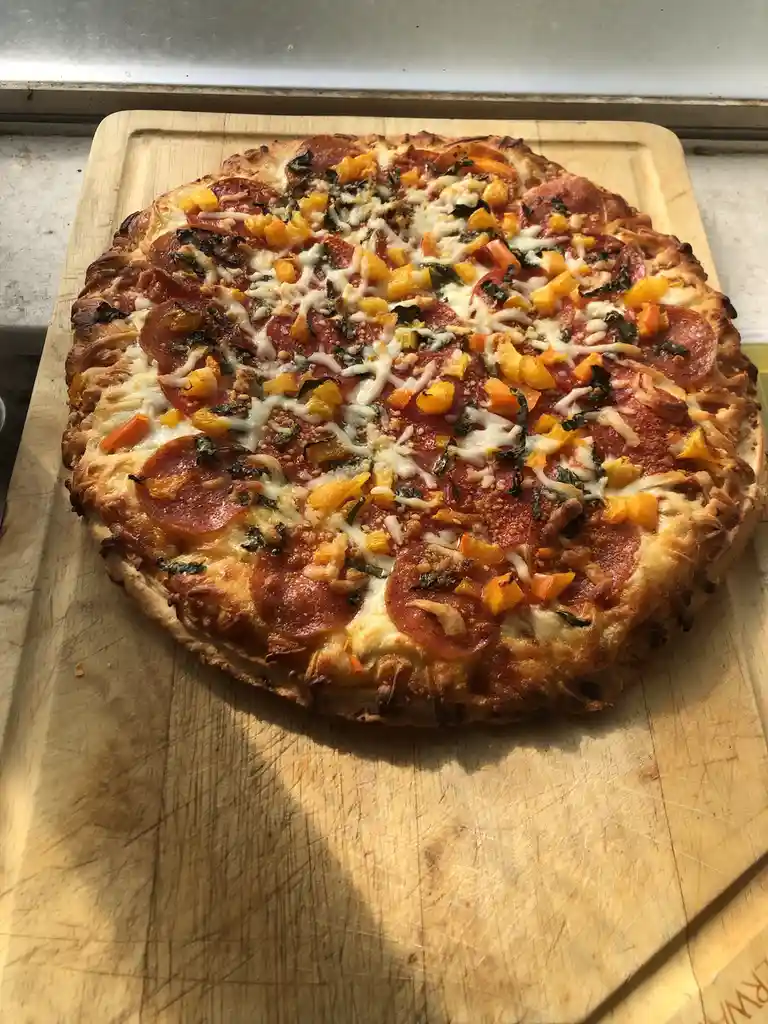 A freshly baked pizza with pepperoni, melted cheese, and diced butternut squash sits on a well-used wooden cutting board…