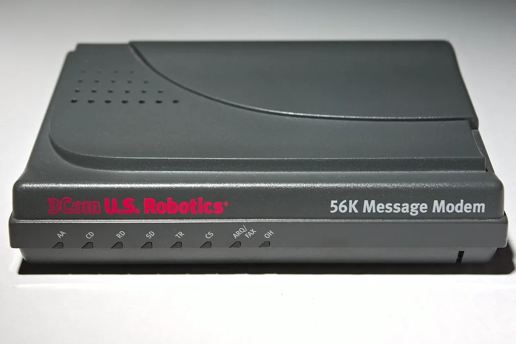 A close-up photo of a gray 3Com U.S. Robotics 56K Message Modem with visible indicator lights labeled AA, CD, RD, SD, TR…