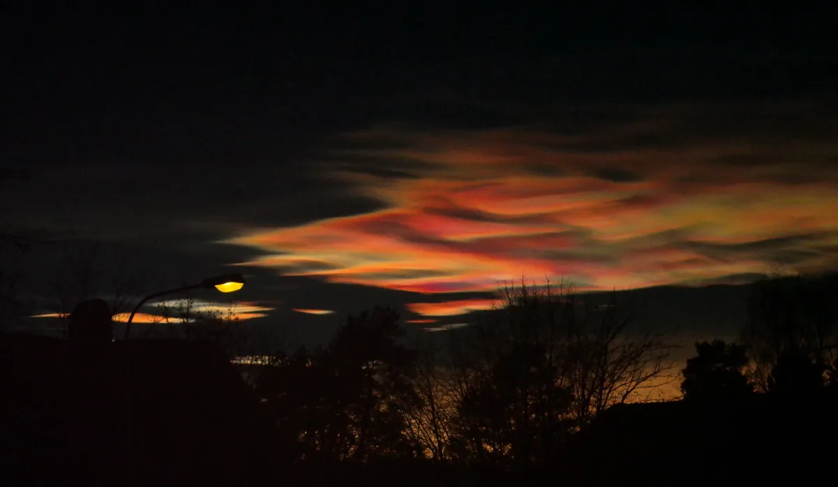 A long-exposure photograph captures a vibrant, streaky sunset or sunrise with fiery orange and red clouds against a dark…