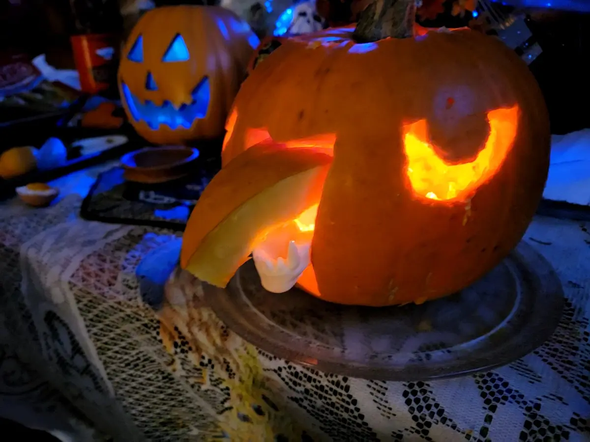 A close-up of a carved Halloween pumpkin with a lit interior, featuring a large, curved mouth and a white plastic tooth…