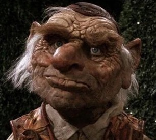 A close-up of a grotesque, wrinkled goblin-like creature with large ears, a bulbous nose, and a smug, slightly sinister…