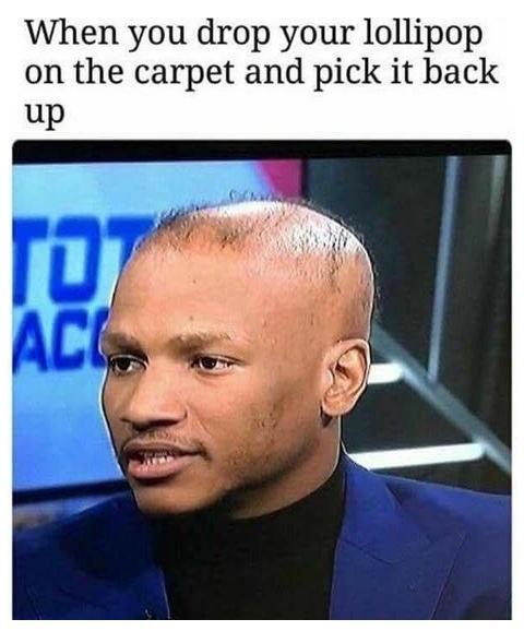 A close-up image of a Black man with a shaved head, wearing a blue suit jacket over a black turtleneck, looking slightly to…