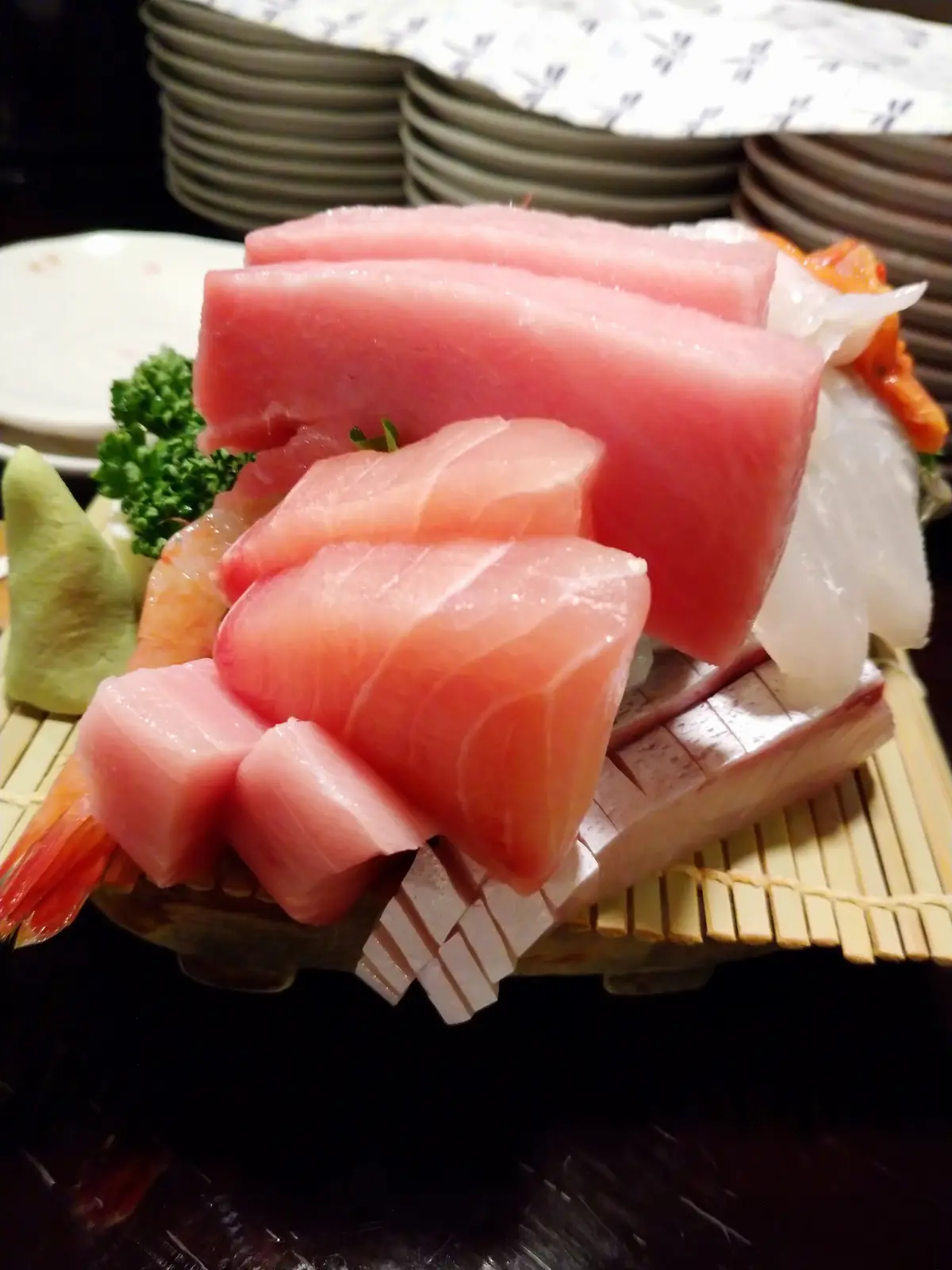 A close-up photo of a platter of fresh sashimi featuring pink tuna slices, shrimp, and white fish arranged on a wooden…