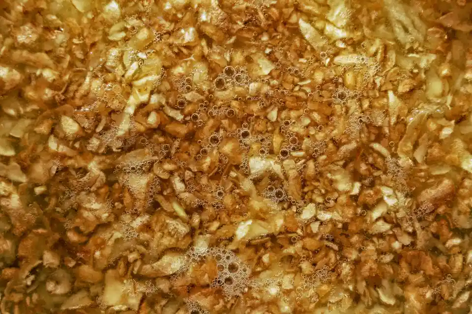The image shows a close-up of oatmeal or porridge simmering in a pot, with visible bubbles and a textured surface of oats…