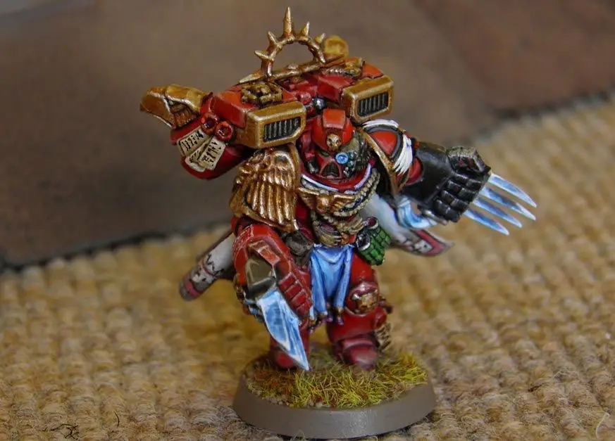 A highly detailed, hand-painted miniature of a red-armored warrior with golden wings, spiked helmet, and multiple weapons…