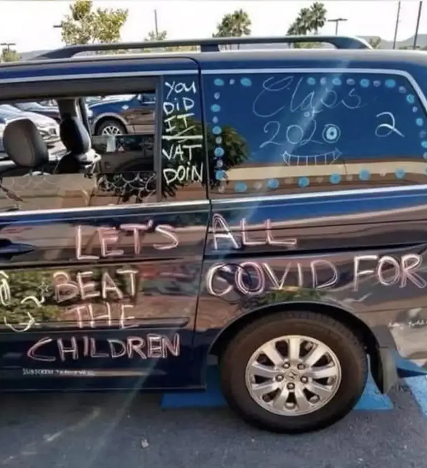 A dark blue van has chalk-style text and drawings on its side and windows. The side reads 'LET'S ALL BEAT COVID FOR THE…
