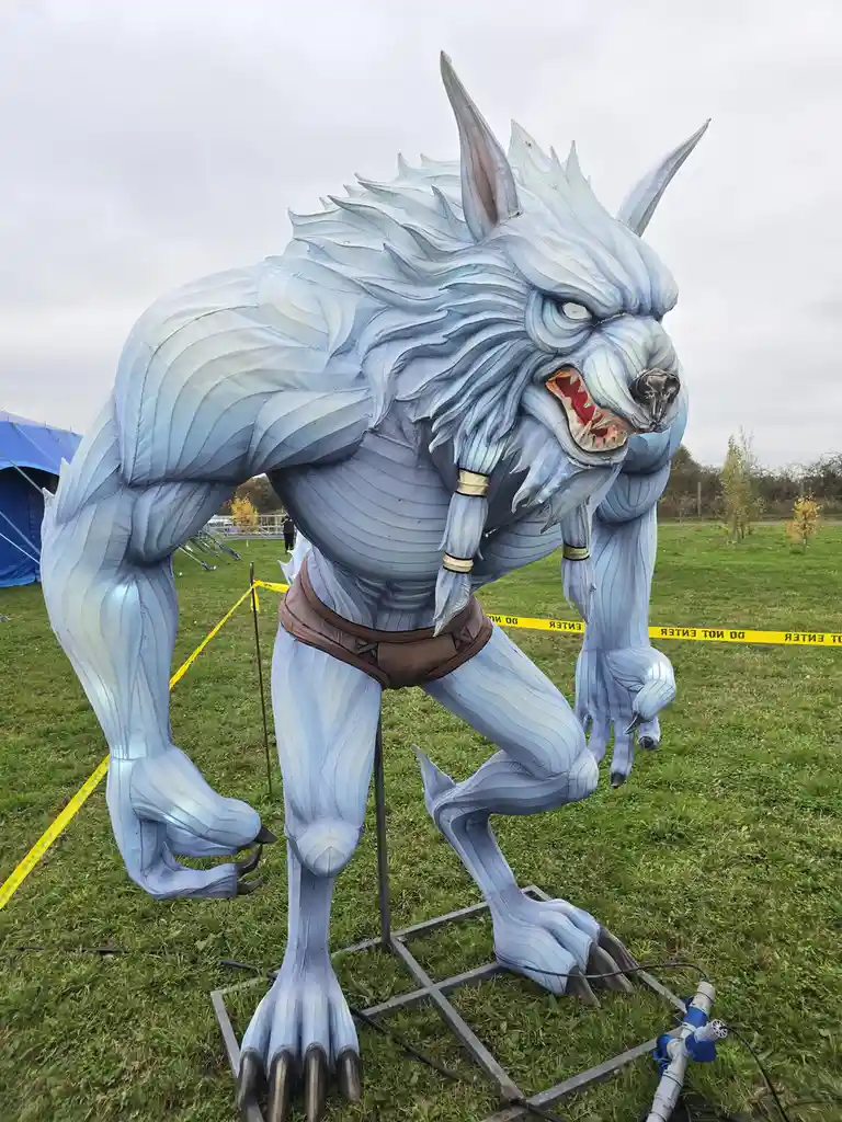 A large, menacing blue werewolf statue with sharp claws and fangs stands on grass, surrounded by yellow 'do not enter'…