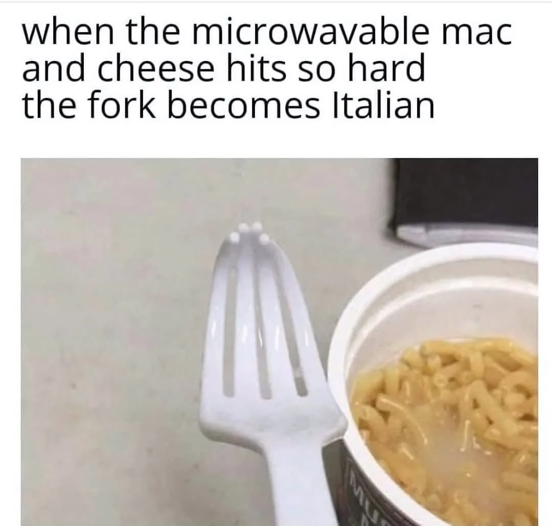 A close-up photo shows a white plastic fork standing upright next to an open container of microwavable macaroni and cheese…