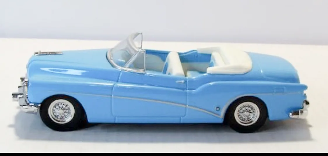 A light blue toy convertible car with white interior and chrome details is shown from the side on a plain white surface. The…