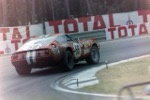 A vintage red race car with number 34 is captured mid-turn on a racetrack, with a large red and white 'TOTAL' advertising…