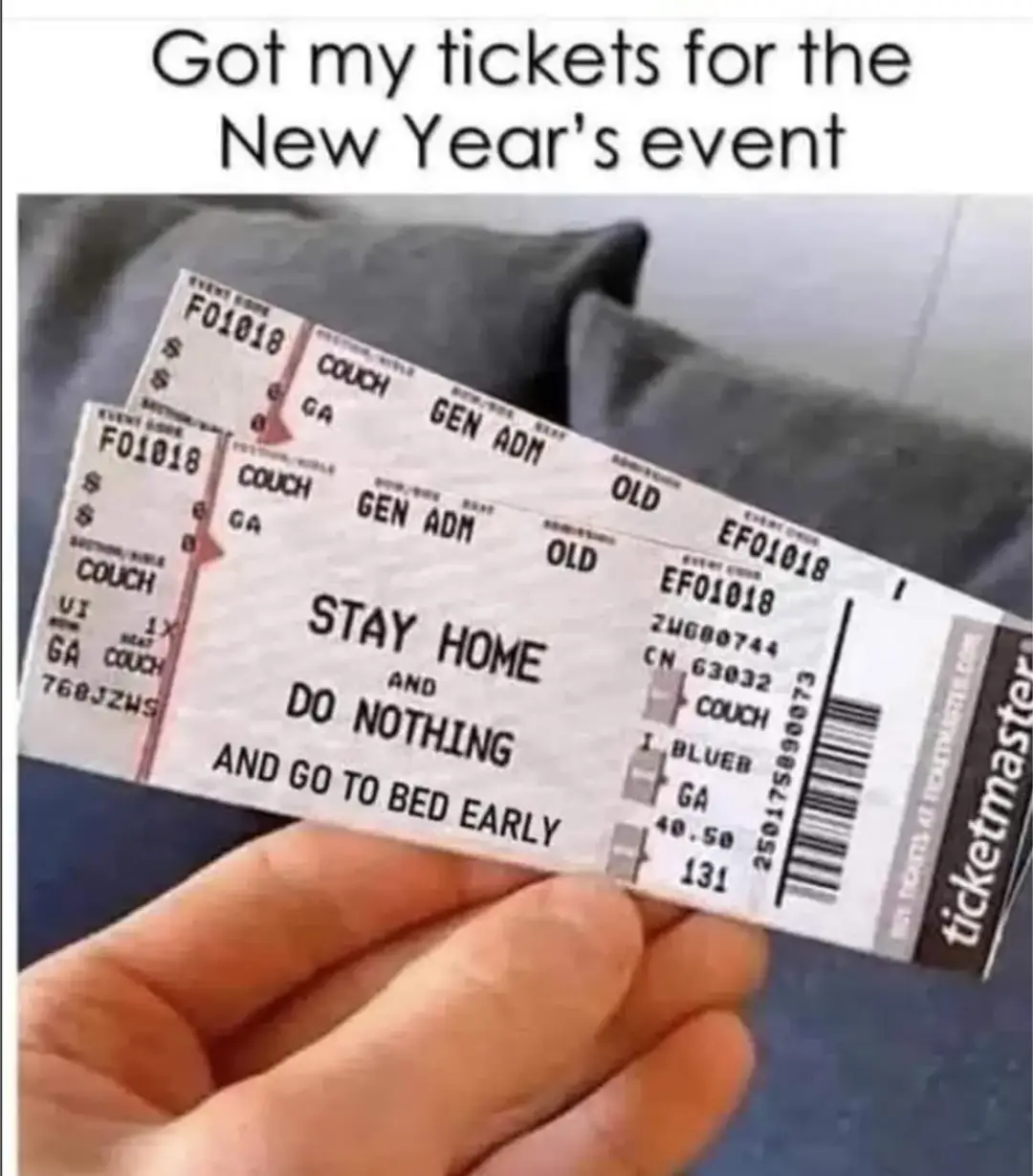 A hand holds two physical event tickets from Ticketmaster, which are visibly printed with the text 'STAY HOME AND DO NOTHING…