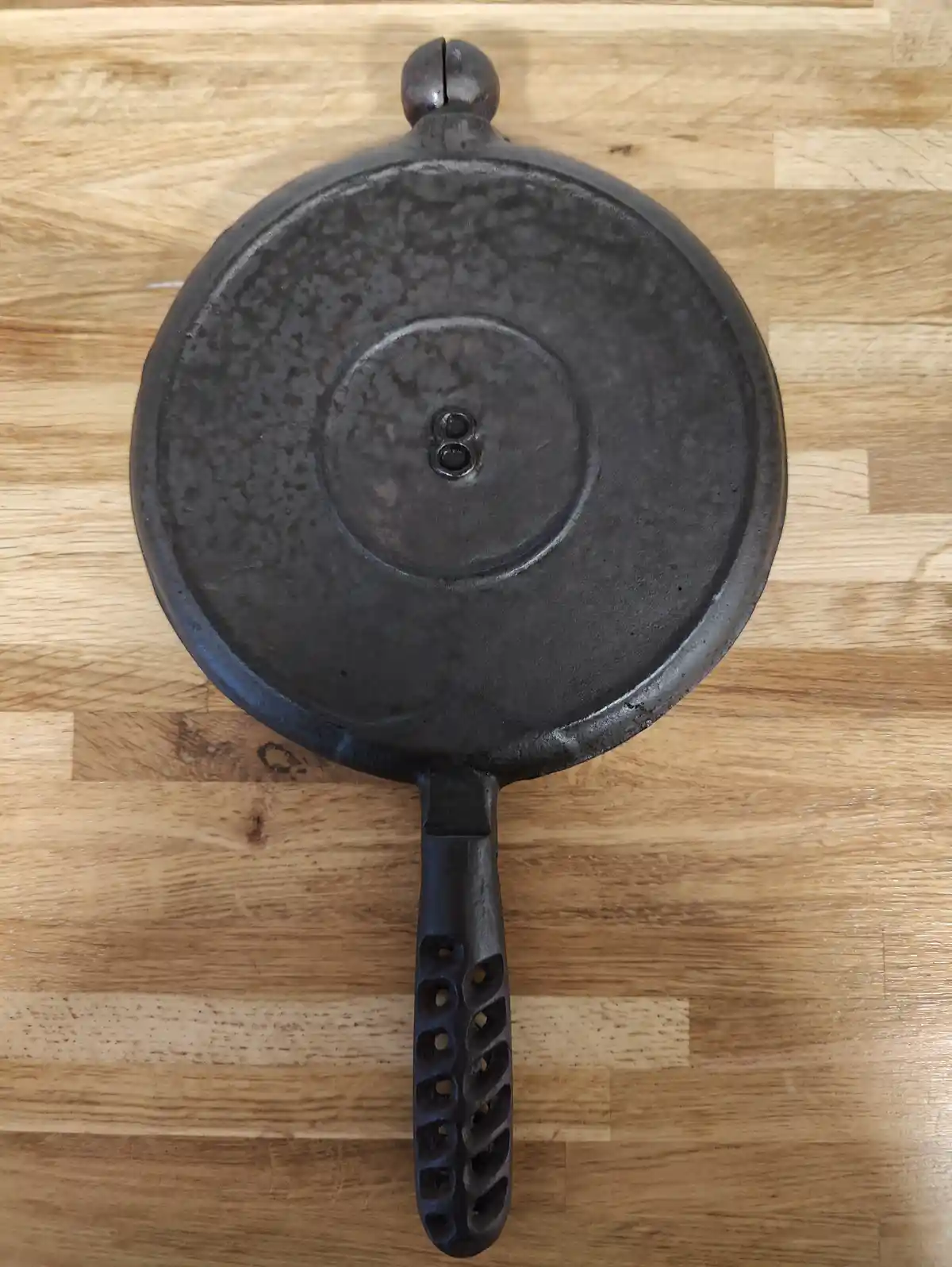 a top-down photo of a black cast iron skillet resting on a light wood surface, featuring a handle with a distinctive…