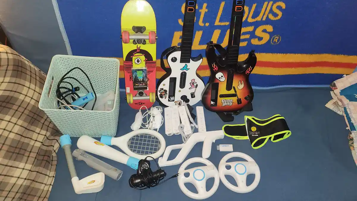 A collection of Nintendo Wii accessories and games laid out on a blue blanket with 'St. Louis Blues' text, including two…