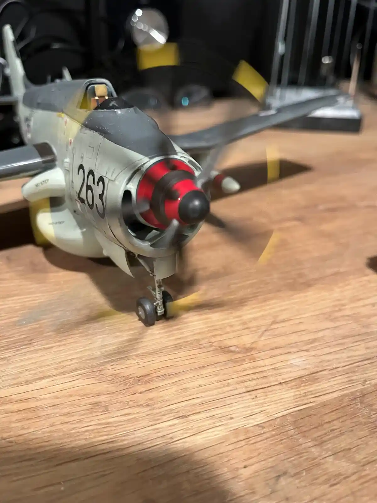 A close-up photo of a detailed model airplane with the number 263 on its side, sitting on a wooden surface. The propeller is…