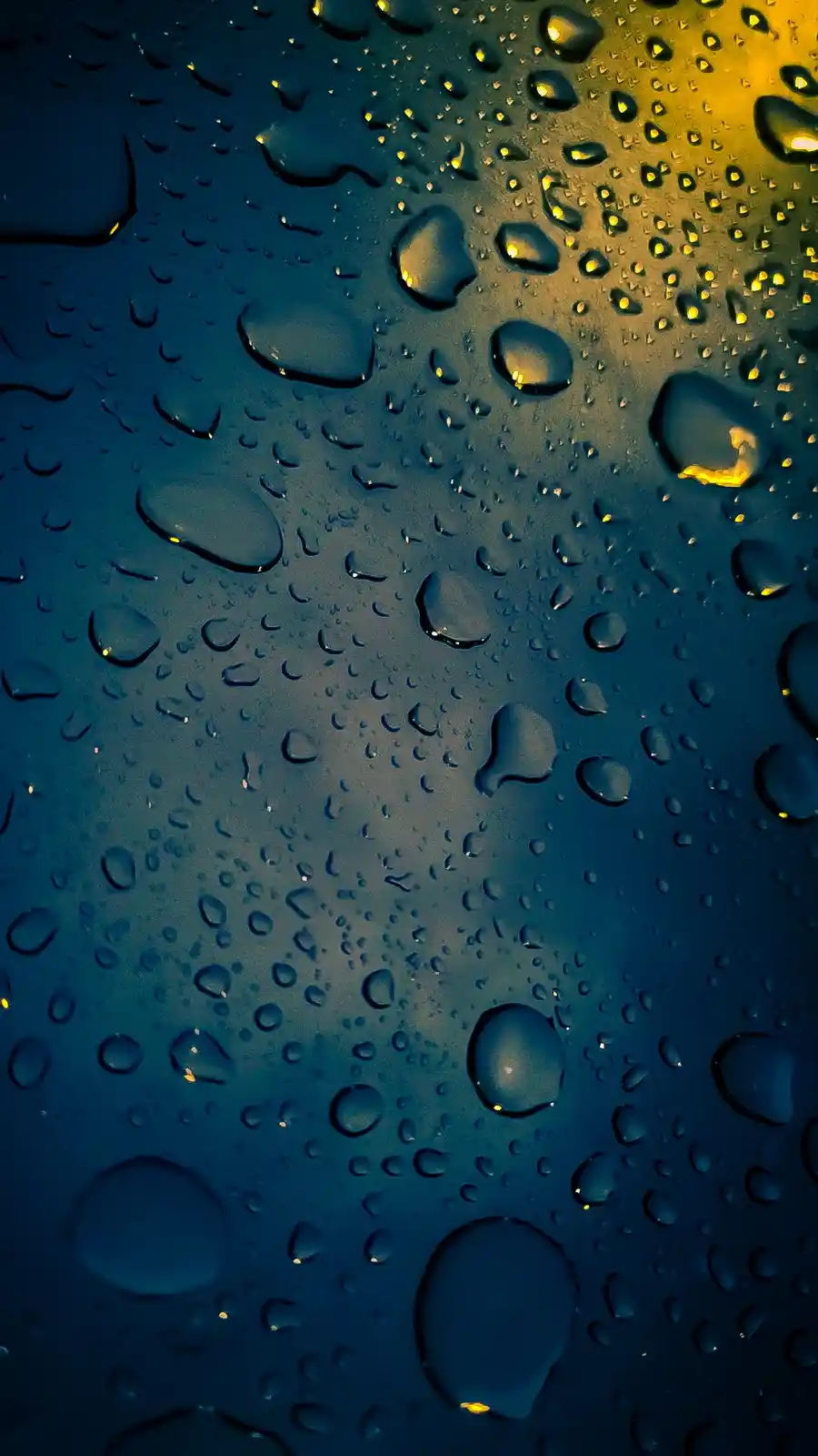 A close-up photo of water droplets on a surface, with a gradient from dark blue to golden yellow light. The droplets vary in…