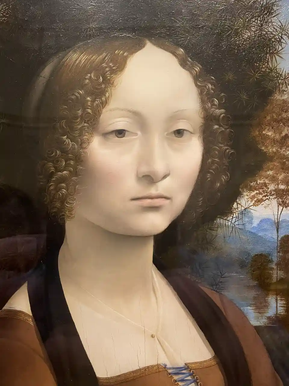 A close-up of a classical Renaissance-style portrait of a woman with curly brown hair, wearing a brown and black garment…