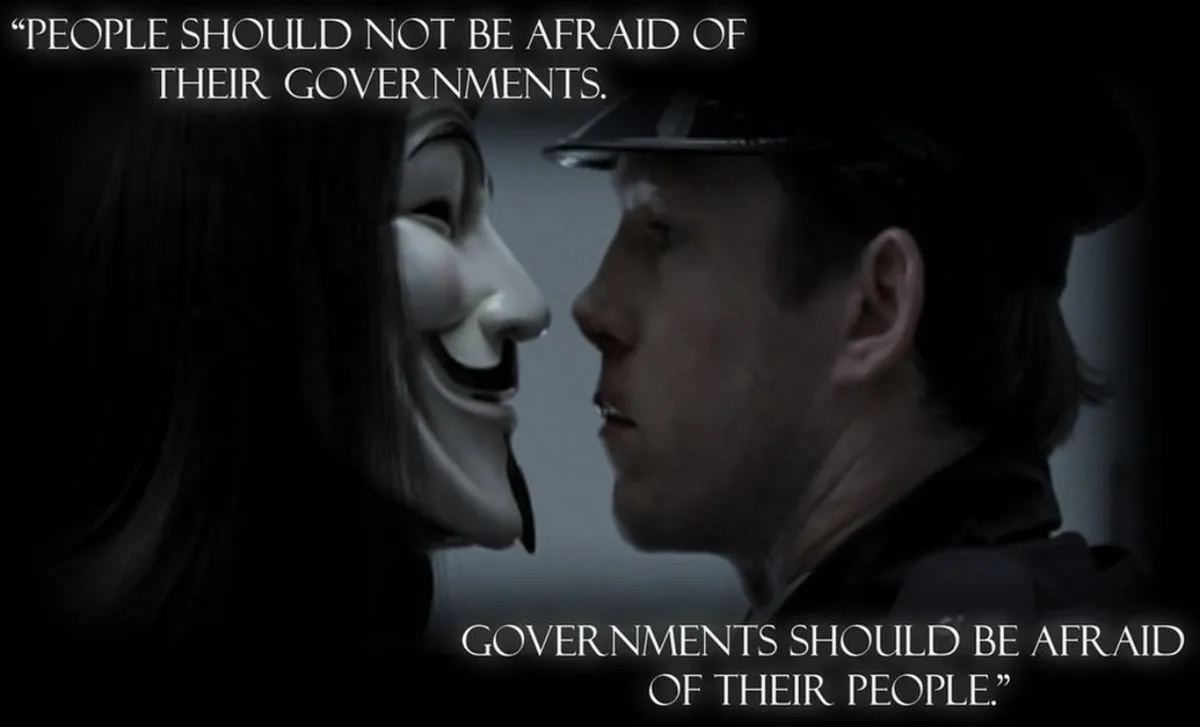 A dark, cinematic image shows a person wearing a white Guy Fawkes mask facing a man in a police-style cap, their faces…