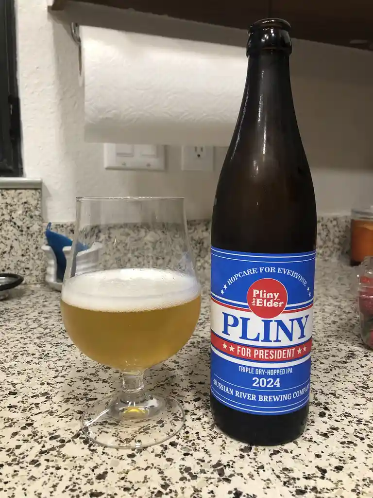 A bottle of Russian River Brewing Company's 'Pliny the Elder' beer sits next to a glass of the poured beer on a speckled…