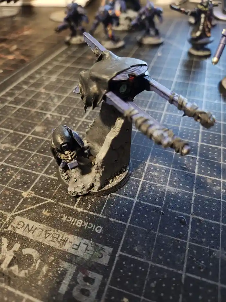A close-up photo of a painted miniature of a Space Marine in a kneeling position beside a large, broken, and crudely…