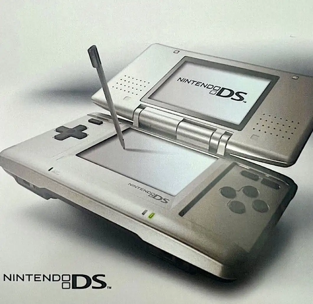A silver Nintendo DS handheld gaming console is shown open, with its stylus hovering over the touchscreen. The top screen…